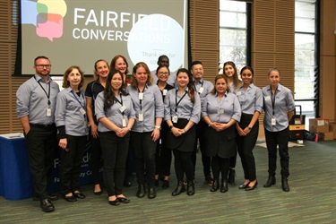 Fairfield City Council staff members who were all part of the Fairfield Conversations Summit team posing for a group photograph in front of a projected PowerPoint slide show