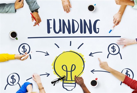 A bunch of hands pointing at large text which says 'funding' above a picture of a light bulb surrounded by dollar symbols