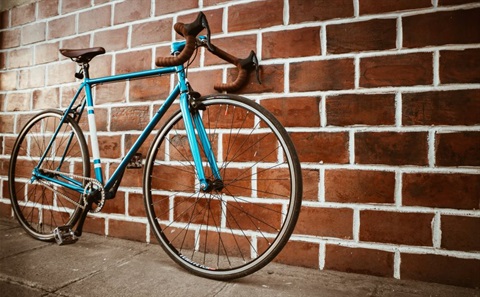 Blue bicycle resting against red brick wall