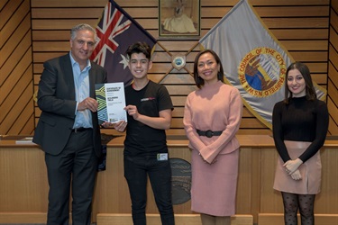 Mayor Carbone handing a certificate of achievement to Alejandro Trejo for entrepreneurial talent while he stands next to Councillors Dai Le and Sera Yilmaz