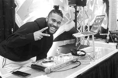 Black and white photograph of DJ DPAK smiling and posing with a peace sign at Bonnyrigg Youth Centre. Photographed by Hannah Teau & Noor Abu-Sada