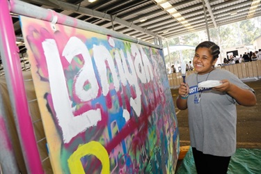 Young girl posing next to graffiti wall holding a paintbrush