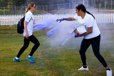 Youth volunteer throwing purple colour powder at female festival-goer