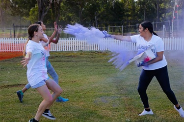 Youth volunteer throwing purple colour powder at young festival-goers