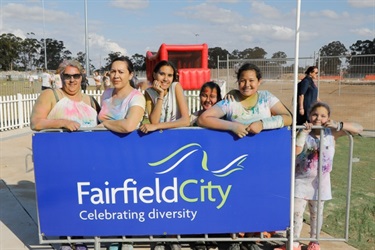 Families covered in colourful powder posing with Fairfield City banner