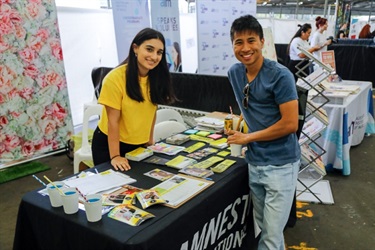 Stallholder and festival go-er smiling and posing at Amnesty stall