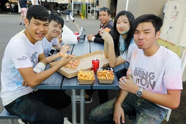 Group of young friends sitting at table eating pizza and fries