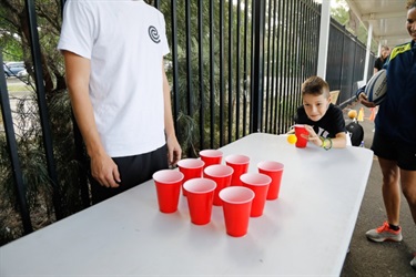 Young boy throwing ping pong balls at red plastic cups