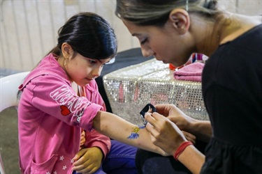 Young girl receiving blue and gold glittery tattoo of a crown with wings