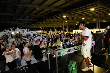 DJ at the turntables in front of a crowd of young people covered in foam