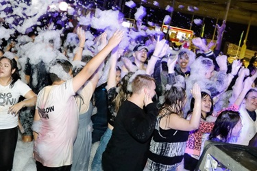 Young people covered in foam and dancing with their arms up on the dance floor