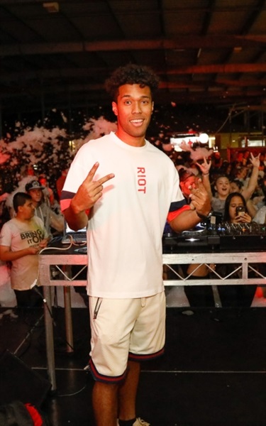 DJ smiling and posing in front of crowd of young people on the dance floor