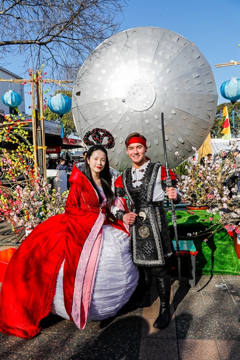 Young woman dressed as the Moon Goddess and young man dressed as the Sun Shooter smiling and posing in front of Cabramatta Moon Festival decorations