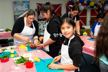 Young girl smiling while chopping herbs on a cutting board at the kid's cooking workshop