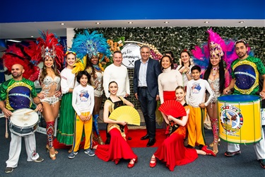 Hon. MP Chris Bowen, Mayor Frank Carbone and Councillor Dai Le smiling and posing with Culinary Carnival performers in front of the festival decorative backdrop