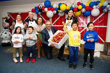 Mayor Frank Carbone and Councillor Dai Le smiling and posing with workshop facilitators and young participants while holding different fruits and vegetables