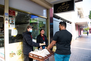 Two volunteers smiling while handing out free bread samples to a young man