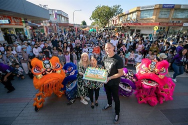 Fast Ed and Angie Hong holding cake with four lions and a large crowd behind