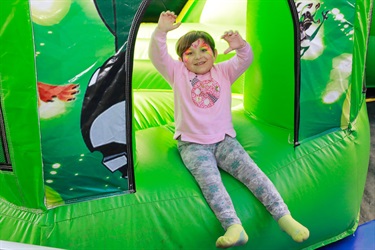 Young girl with butterfly face paint smiling and sitting at entrance of green jumping castle