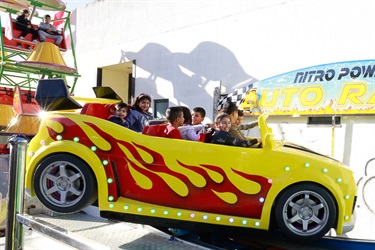 Young children smiling while riding on yellow car ride and small green ferris wheel