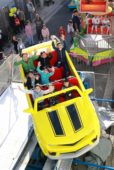 Young children smiling and raising their arms in the air while riding yellow car ride
