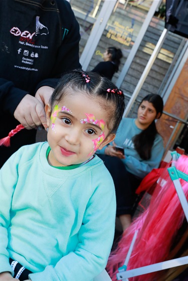 Young girl with pink and yellow floral face paint getting her hair braided