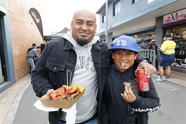 Man and young boy smiling and posing holding a box of assorted meat and chips