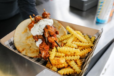 Box of skewers with sauce, chips and flat bread