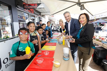 Mayor Frank Carbone and Councillor Dai Le posing with young children wearing aprons in front of colourful cutting boards