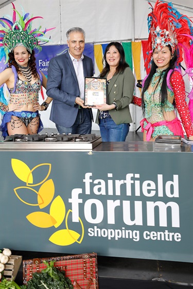 Mayor Frank Carbone and young woman smiling and holding a certificate while posing with two female Brazilian dancers