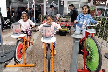 Three young girls smiling and posing while riding on pedal powered smoothie bicycles