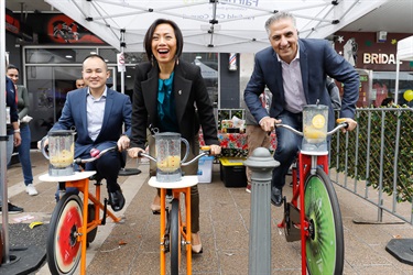Mayor Frank Carbone, Councillor Dai Le and Councillor Adrian Wong smiling and posing while riding pedal powered smoothie bicycles