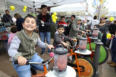 Three young children smiling and posing while riding pedal powered smoothie bicycles
