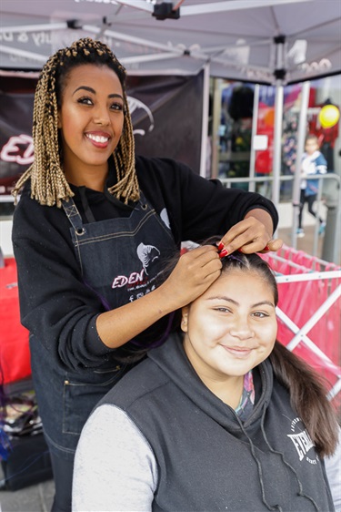 Young woman smiling and posing while braiding girl's hair