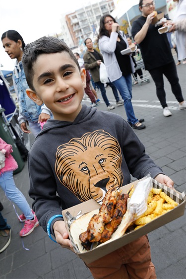 Young boy smiling and posing while holding box of skewers, chips and flat bread