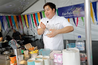 Master Chef contestant Bryan Zhu smiling and standing behind a table of cooking utensils while stirring batter with a whisk