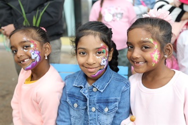 Three young girls smiling and posing with unicorn and floral face paint