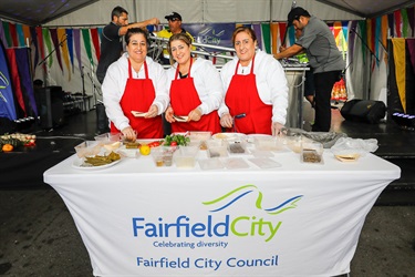 Three women wearing red aprons smiling and posing while preparing food