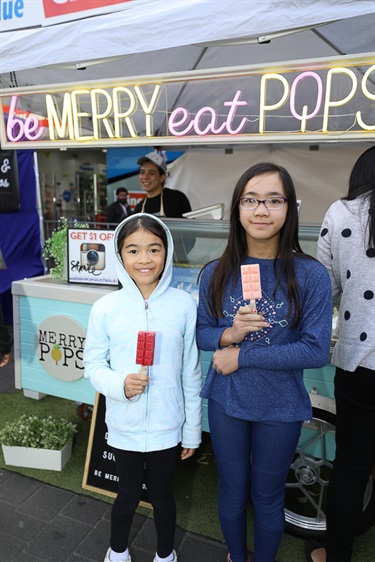 Two young girls smiling and posing holding red and pink ice pops