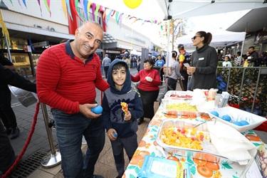 Man and young boy smiling and posing while holding a yellow and red fruit skewer
