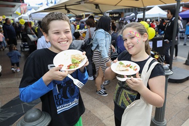 Young boy and girl smiling and posing while holding plates of wraps with vegetables
