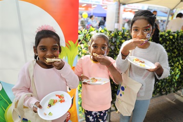Three young girls with colourful face paint eating their wraps