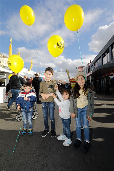 Four young children smiling and posing while holding bright yellow balloons