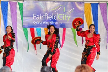 Three young women in red, black and gold costumes performing dance on stage