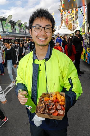 Young man smiling and posing while holding a box of assorted meats and a fruit soda