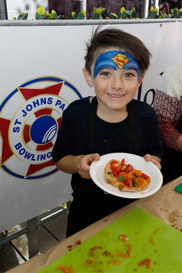 Young boy with superhero face paint smiling and posing while holding a plate of bread with sliced cherry tomatoes