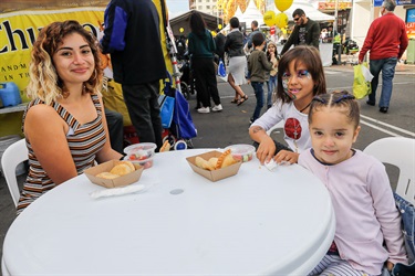 Woman smiling and posing two young girls sitting around a table about to eat empanadas and salad
