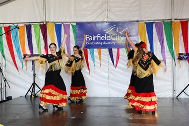 Four young women in red, black and gold costumes performing Spanish dance on stage