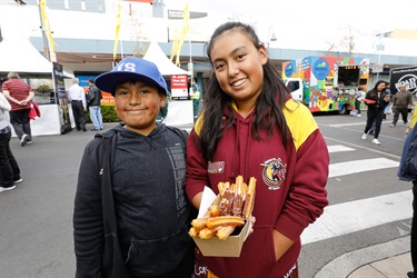 Two young children smiling and posing while holding a box of churros