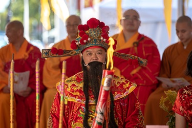 Man dressed in traditional red Chinese clothing and head wear looking at burning candle